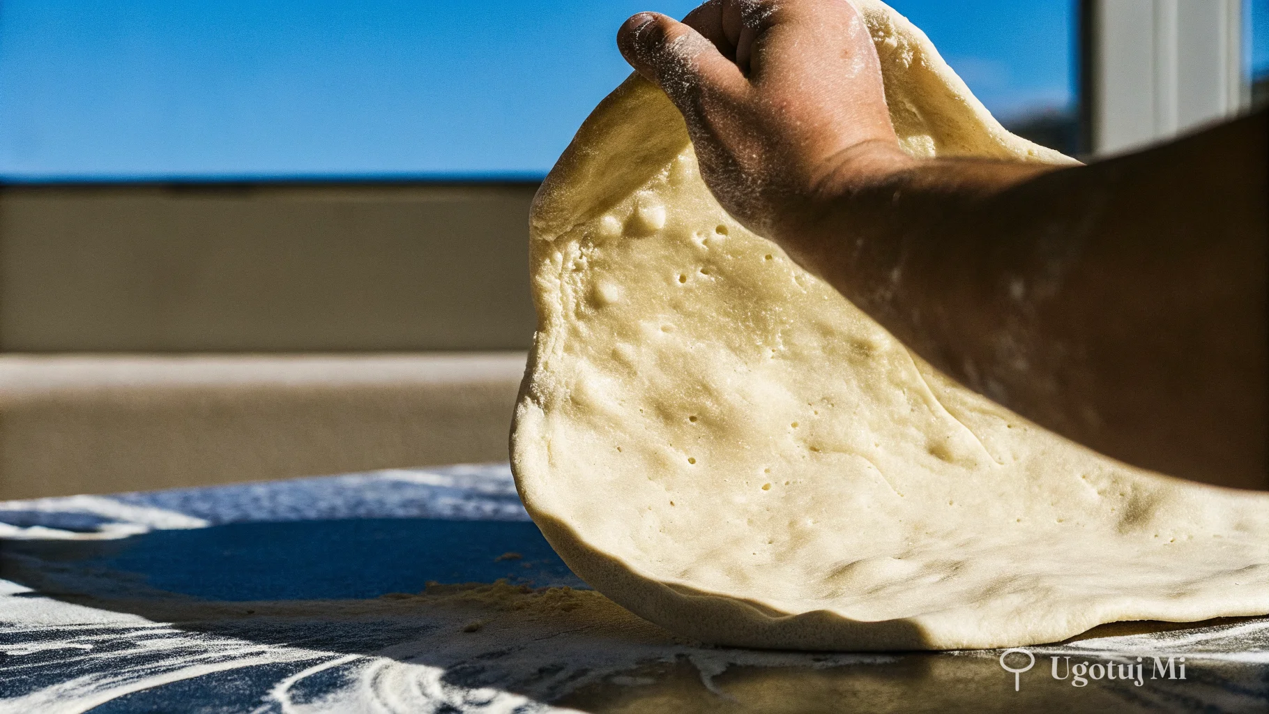 Rozciągane ciasto na pizzę na marmurowym blacie pokazujące elastyczną strukturę | ugotujmi.pl