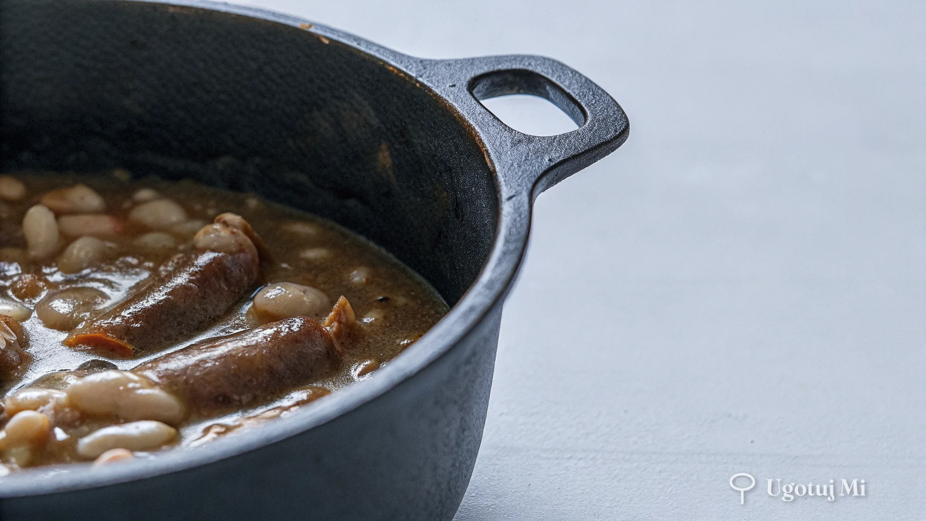 Zbliżenie na gęsty sos pomidorowy z fasolą i kiełbasą gotujący się w garnku | ugotujmi.pl