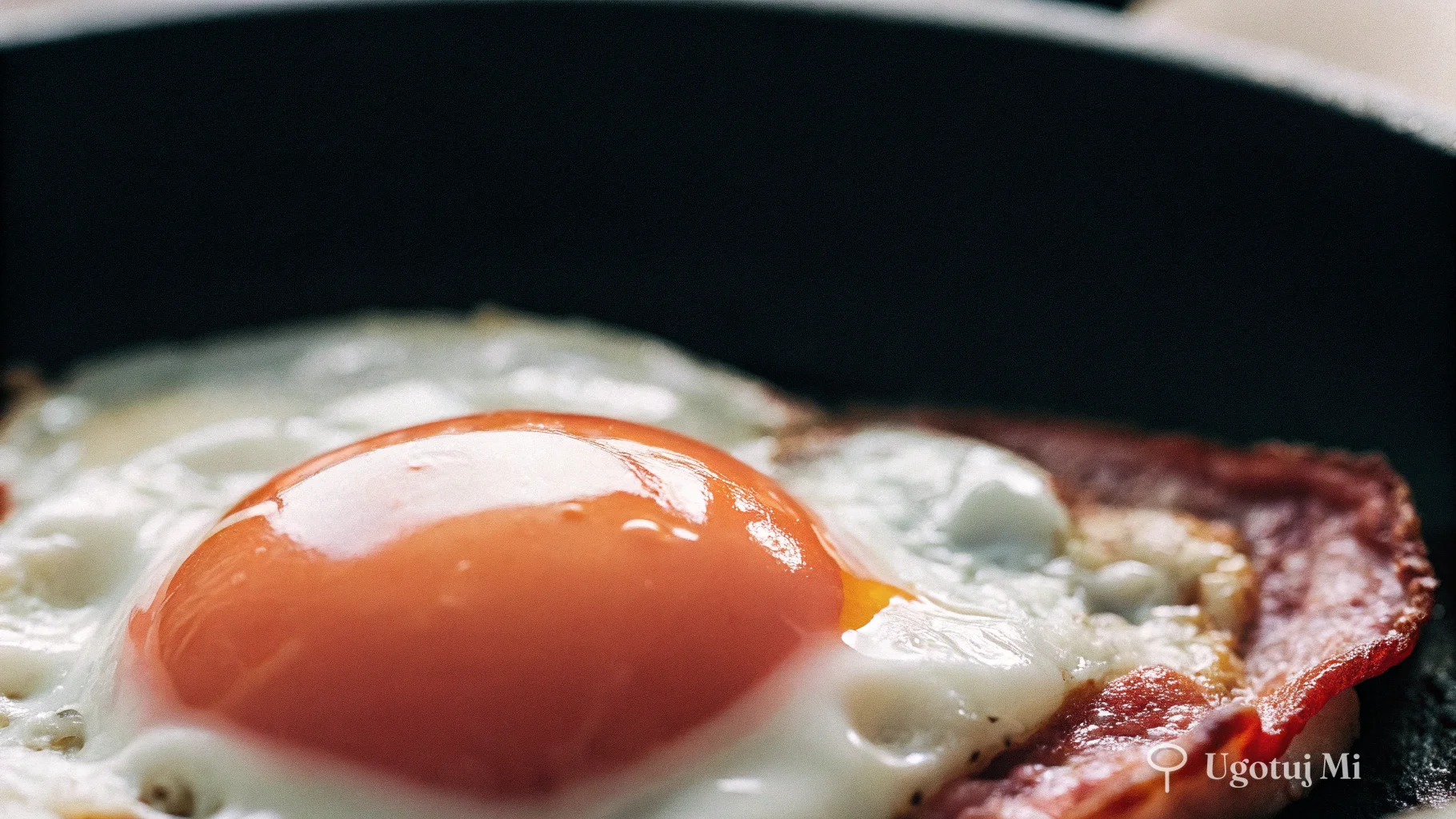 Zbliżenie na błyszczące żółtko jajka sadzonego z chrupiącymi brzegami białka | ugotujmi.pl
