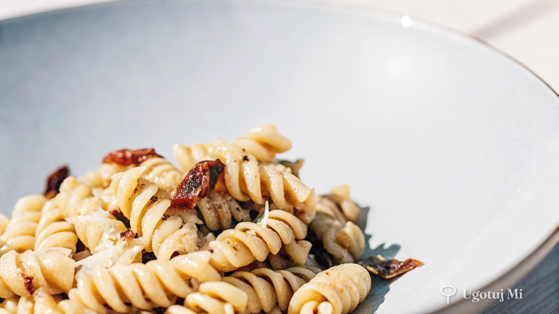 Zbliżenie na makaron fusilli pokryty pesto z kawałkami suszonych pomidorów i wiórkami parmezanu | ugotujmi.pl