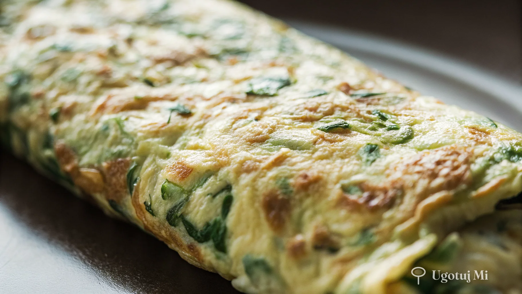 Zbliżenie na puszystą teksturę omleta z widocznymi kawałkami ziół | ugotujmi.pl