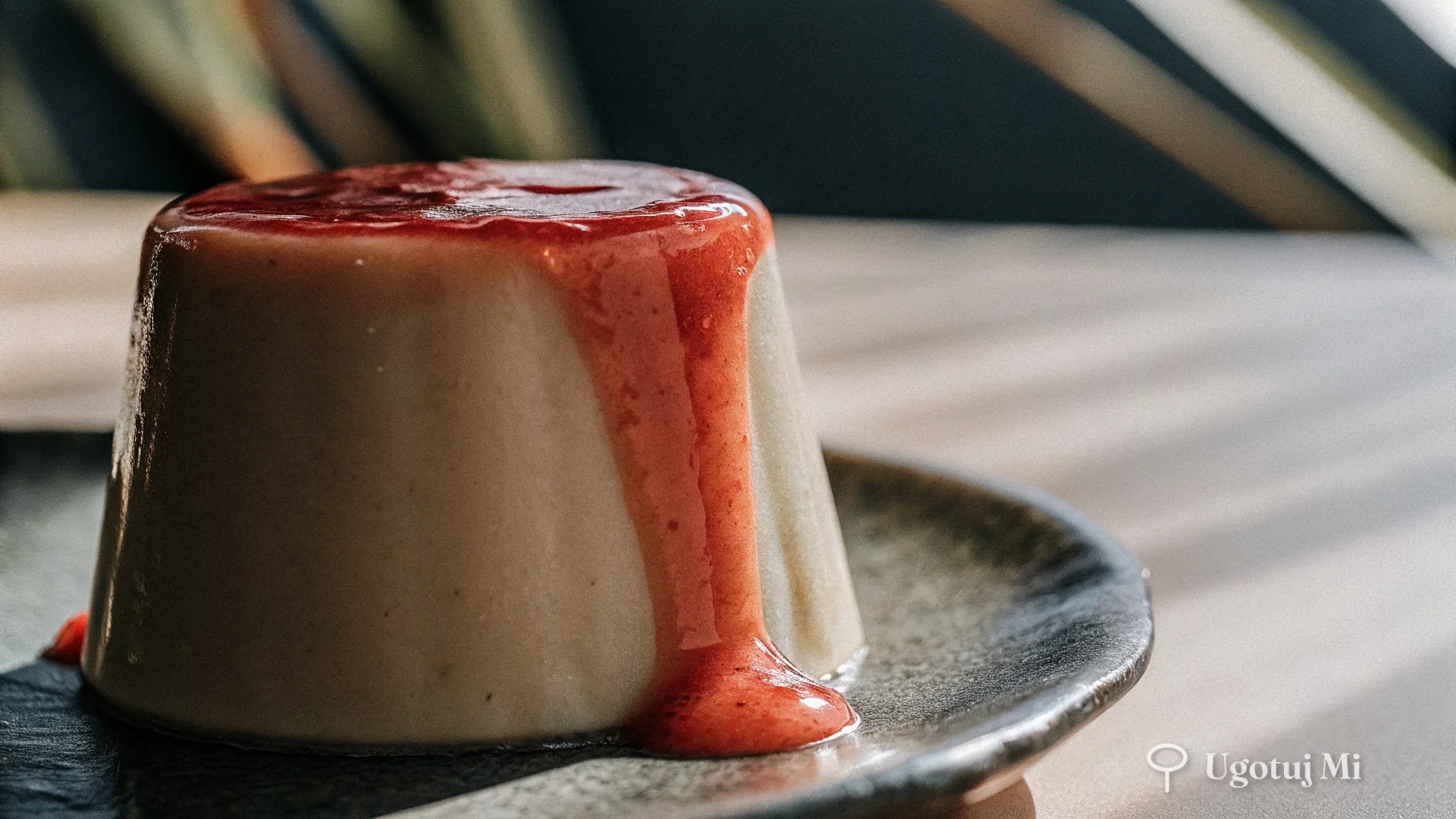 Zbliżenie na jedwabistą teksturę panna cotty z sosem truskawkowym spływającym po boku | ugotujmi.pl