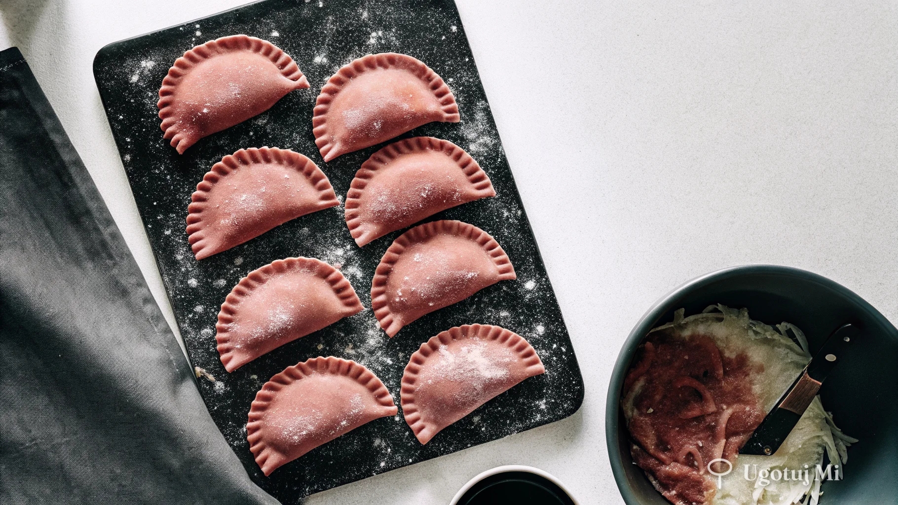 Surowe uformowane pierogi na posypanej mąką desce obok miski z farszem | ugotujmi.pl