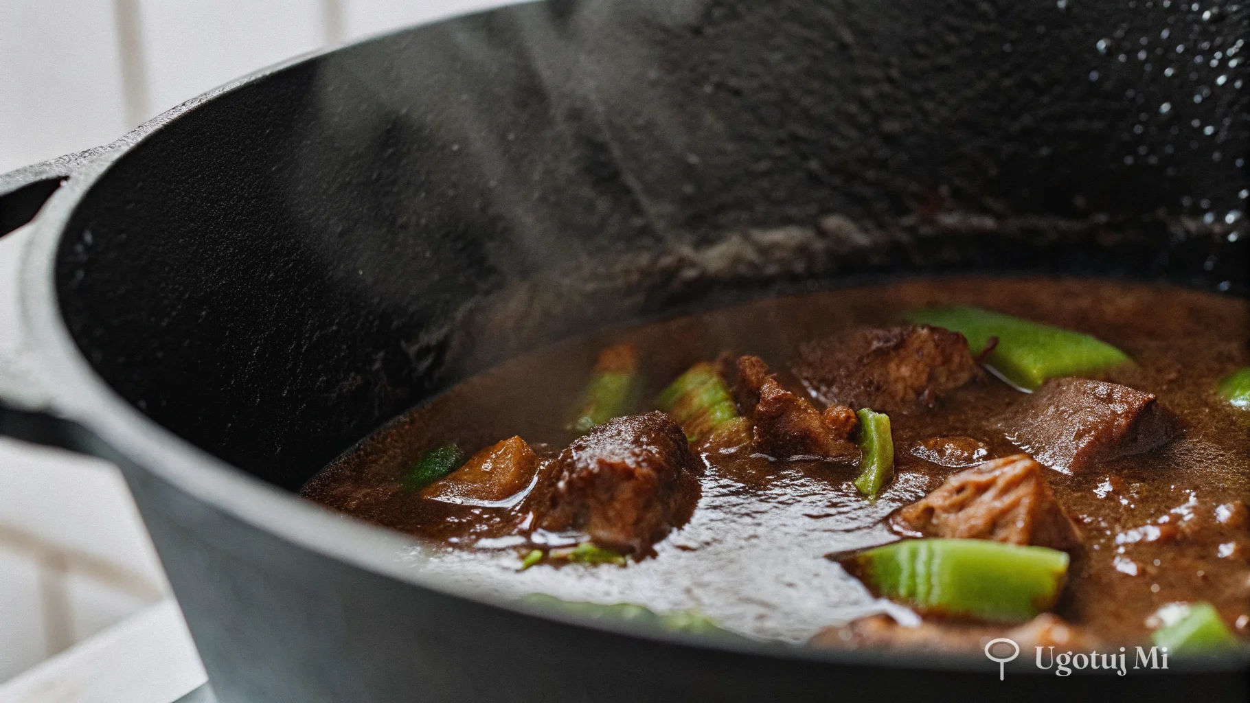 Zbliżenie na gęsty, ciemny sos do żeberek w żeliwnym garnku z kawałkami mięsa | ugotujmi.pl