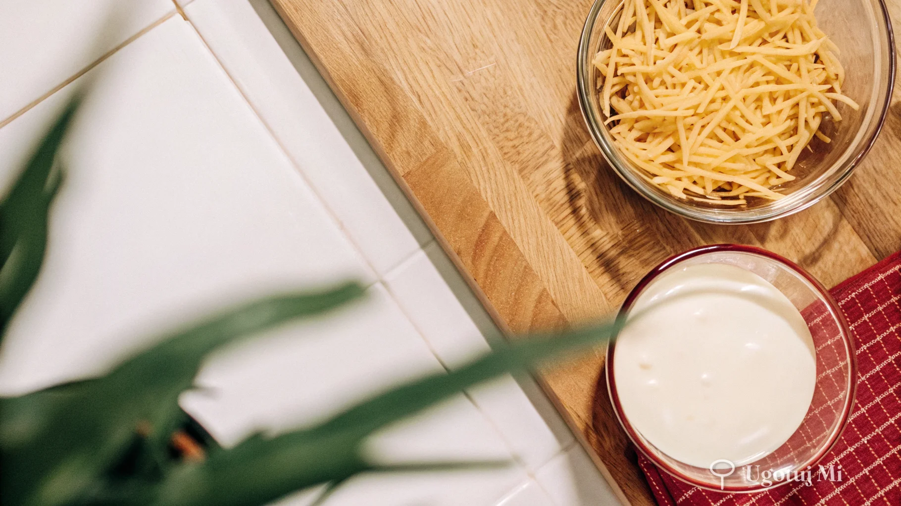 Starty cheddar w misce obok garnka z białym sosem na drewnianym blacie | ugotujmi.pl